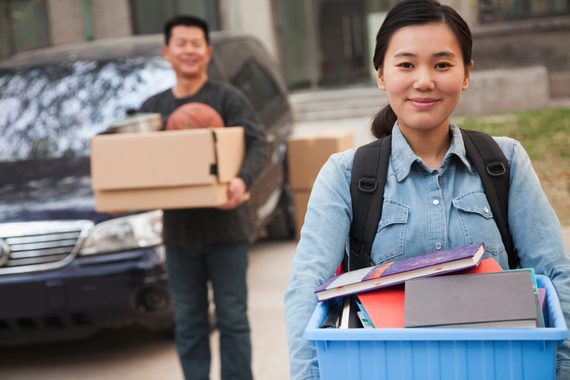 Young woman carrying bin with father behind carrying box as move into college, for College Expenses & Divorce turn to child support attorney Dayton.