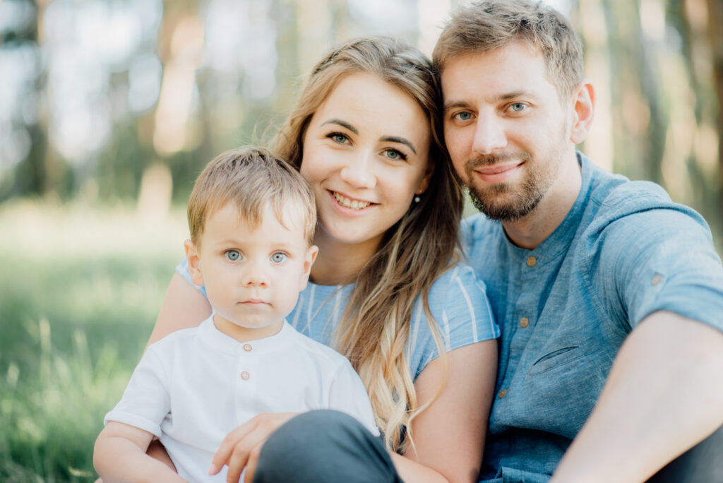 Custody Without Marriage A woman, man, and young boy—possibly navigating custody for unmarried parents in Dayton—sit closely together outdoors, smiling at the camera with green grass and trees in the background.